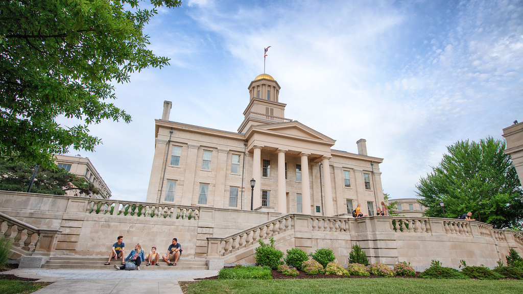 Image of back of Old Capitol building on sunny day with blue sky, scattered white clouds, green grass, and green mature trees.